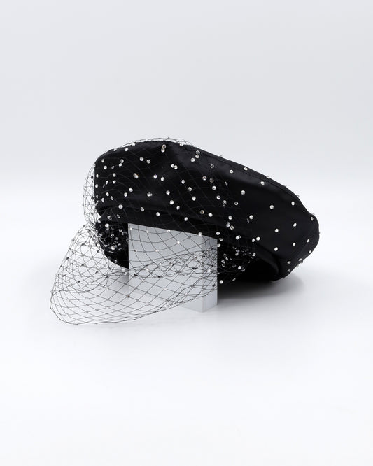 black faux leather beret with crystal embellishments and black veil sitting on top of white wooden panel to show form